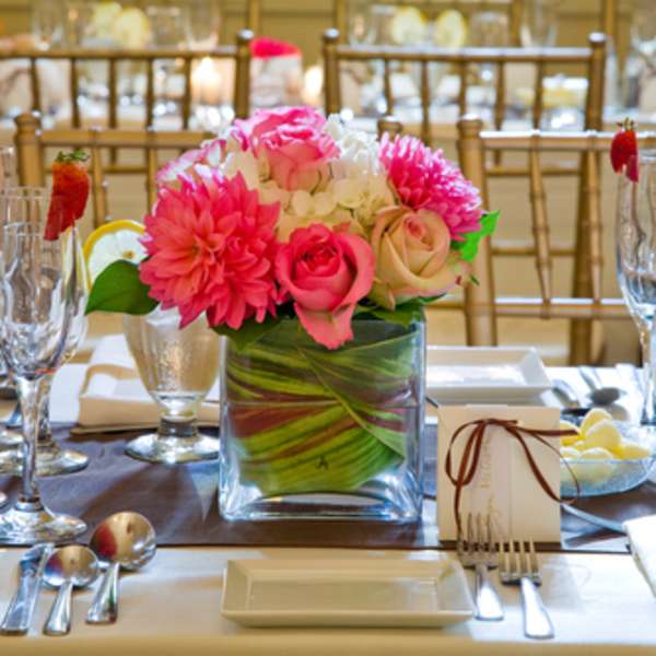 Pink floral centerpiece in a square glass vase on a set dining table