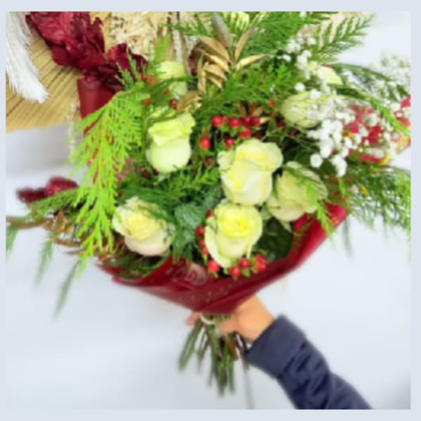 Handheld bouquet of pale yellow roses with red berries and greenery