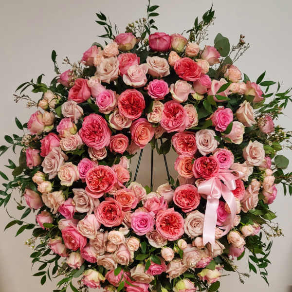 Large pink rose wreath on a black stand with a pink ribbon