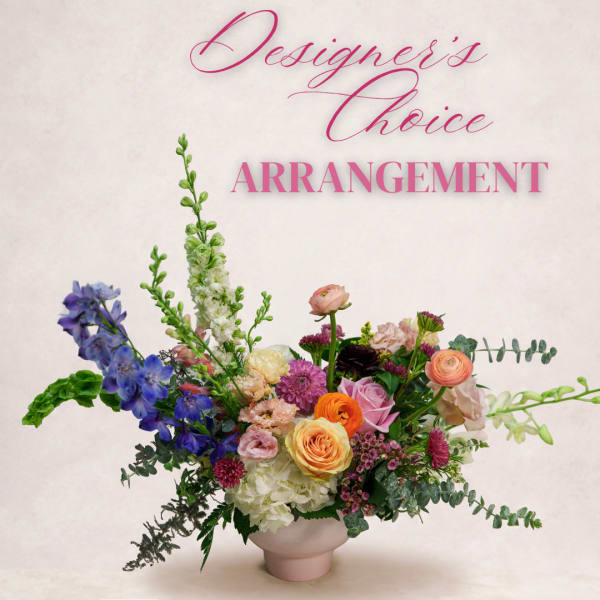 Colorful mixed flower arrangement in a pale vase with tall blue blooms