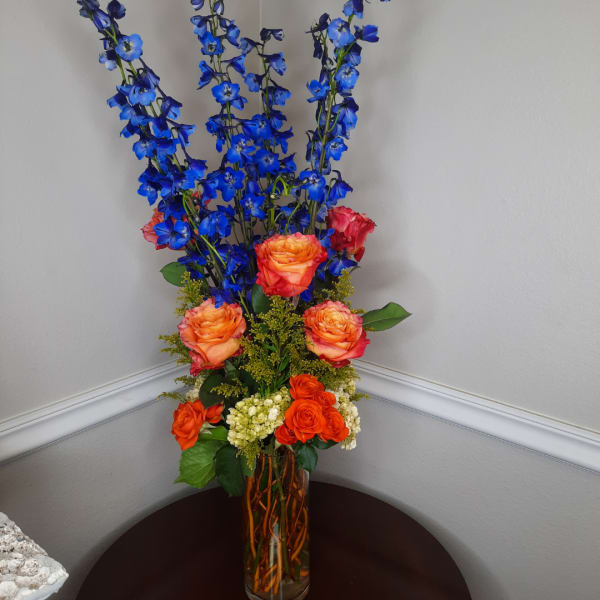Tall bouquet of blue flowers and orange roses in a glass vase