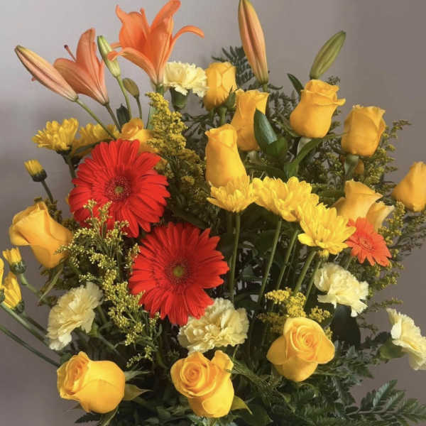 Mixed bouquet of yellow roses, red gerberas, and orange lilies in a blue vase