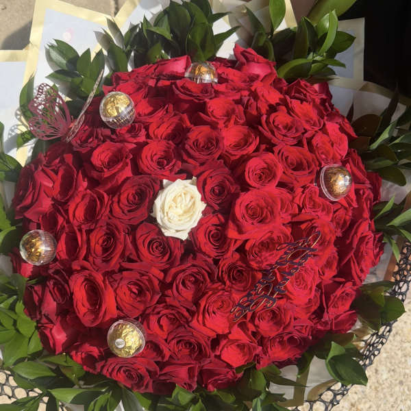 Round bouquet of red roses with one white rose and green foliage