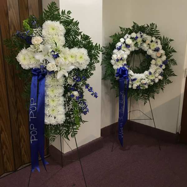 Two white floral funeral wreaths on stands with blue ribbons