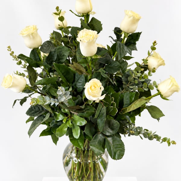 White roses in a clear glass vase with dark greenery