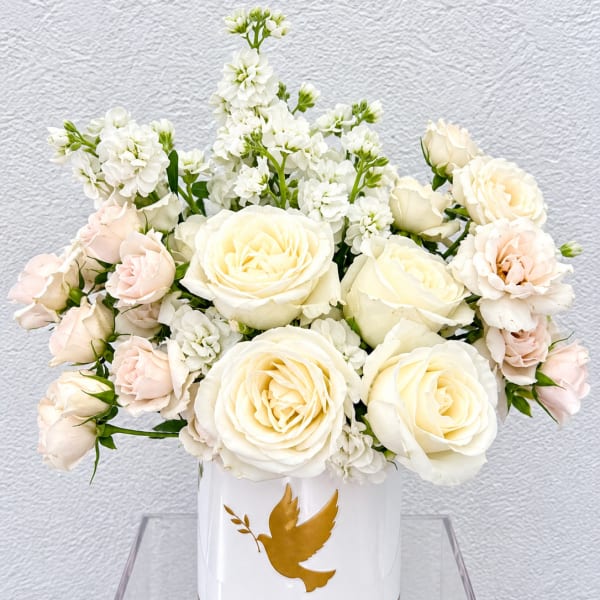 White and blush roses arranged in a white vase with a gold dove emblem
