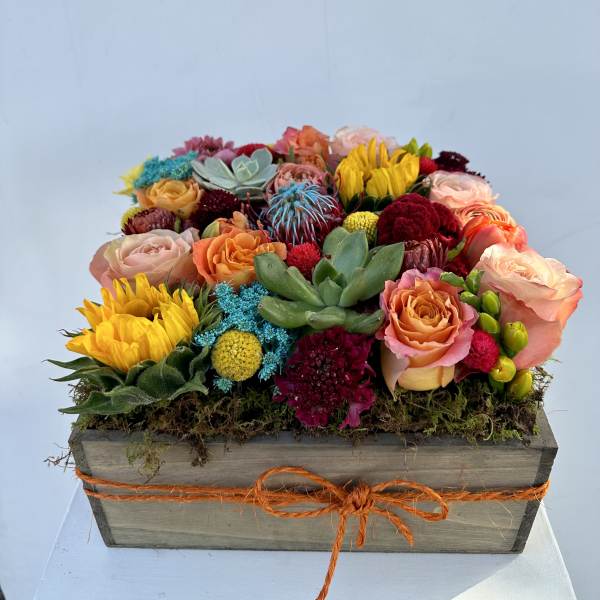 Colorful mixed flower arrangement in a wooden box with an orange ribbon