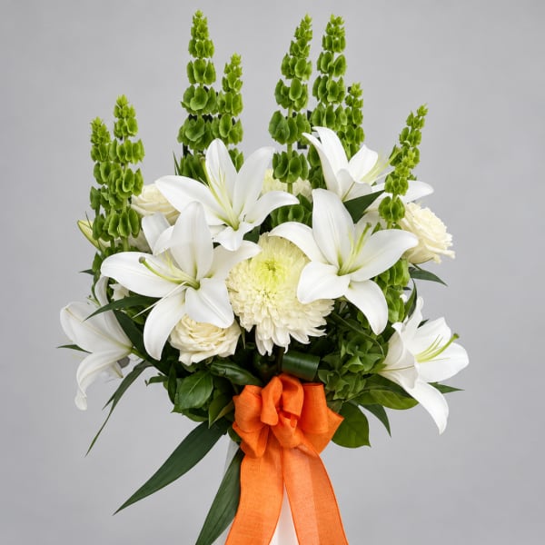 White lilies and cream flowers with tall green spikes, tied with an orange ribbon