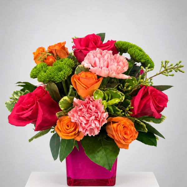 Bright mixed bouquet of roses, carnations, and green mums in a pink vase