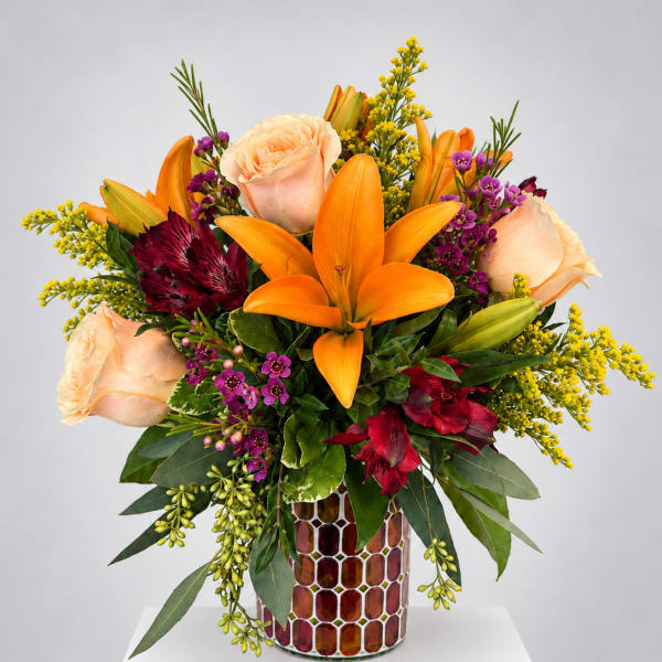 Orange lilies and peach roses in a mosaic vase