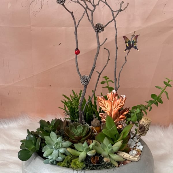 Succulent arrangement in a low round planter with decorative branches and small ornaments.