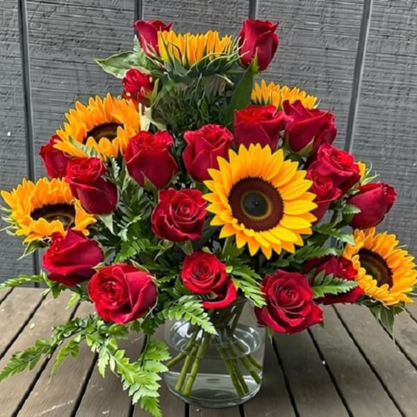 Red roses and sunflowers arranged in a clear glass vase
