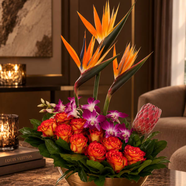 Tropical arrangement with orange bird-of-paradise, roses, and orchids in a gold bowl