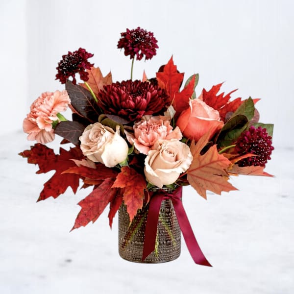 Autumn bouquet of roses and carnations in a textured vase with a ribbon
