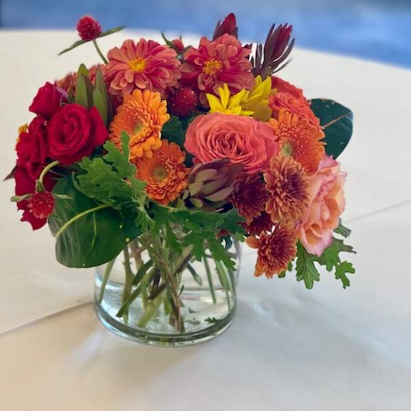 Mixed bouquet of red, orange, and pink flowers in a clear glass vase