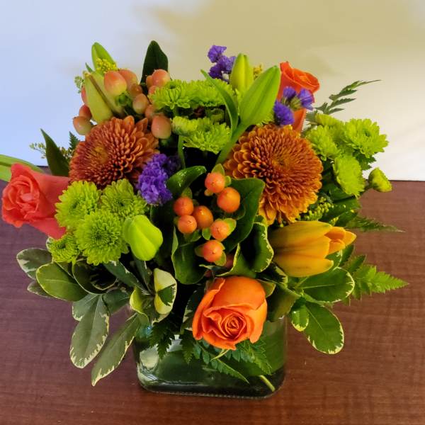 Orange roses and green chrysanthemums in a square glass vase