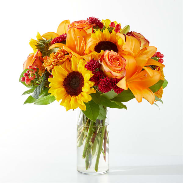 Bouquet of sunflowers, orange lilies, and roses in a clear glass vase