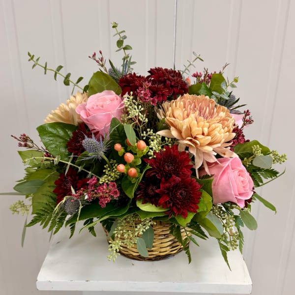 Basket arrangement of pink roses, burgundy mums, and peach blooms