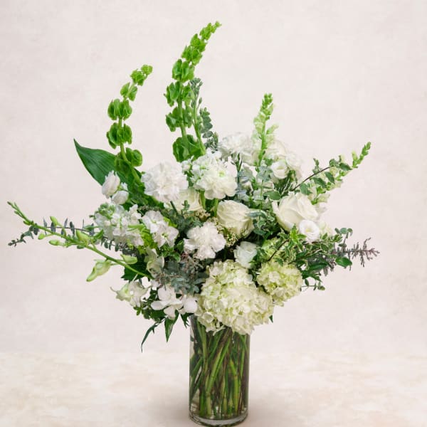 White floral arrangement in a clear glass vase with tall green spikes