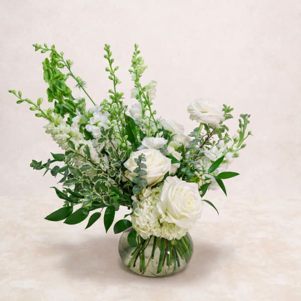 White rose arrangement in a round glass vase with tall green stems
