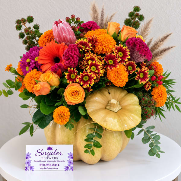 Autumn floral arrangement in a pumpkin-shaped container with orange and pink blooms