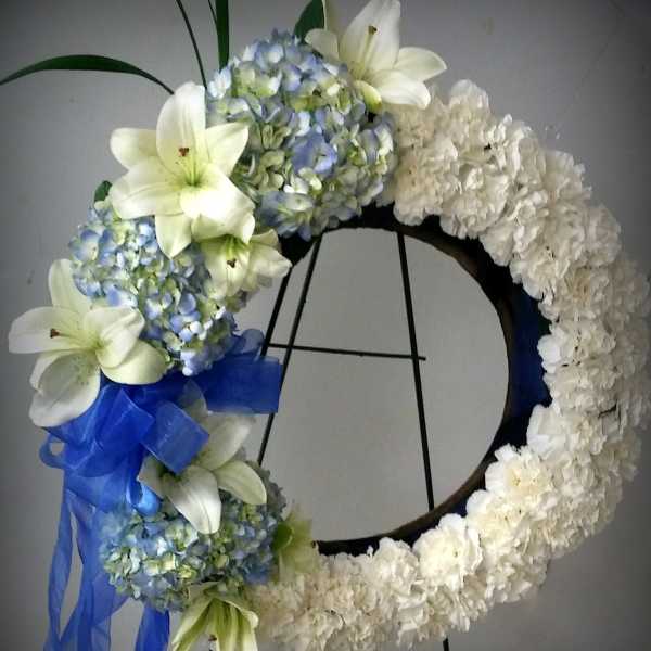White floral wreath with blue hydrangeas, lilies, and a blue ribbon