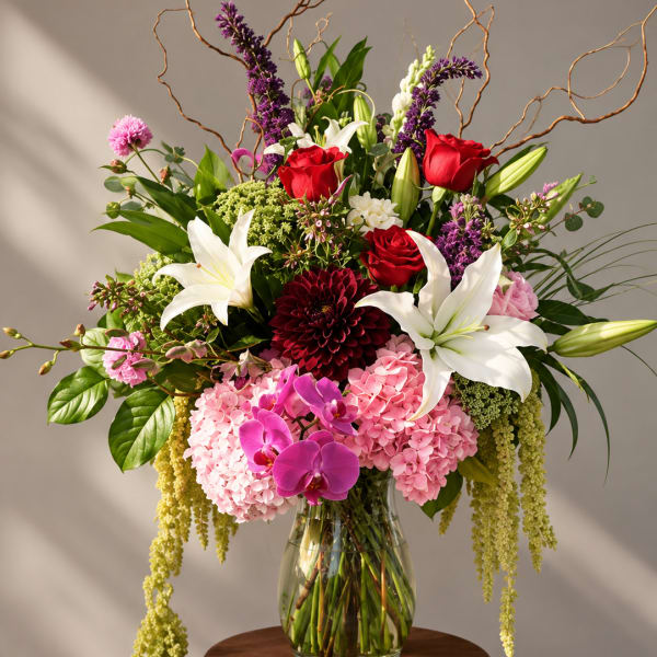 Large mixed bouquet with red roses, white lilies, pink hydrangeas, and orchids in a glass vase