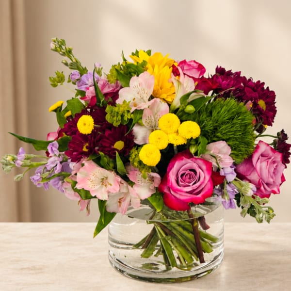 Mixed bouquet of roses, daisies, and alstroemeria in a clear glass vase