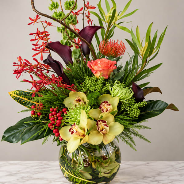 Tropical floral arrangement in a glass vase with orchids, calla lilies, and red accents