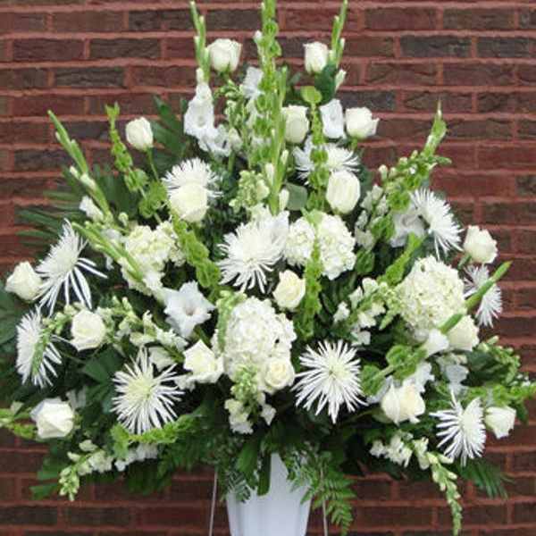 White floral funeral spray in a white container on a stand
