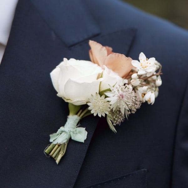 Boutonniere with white and peach flowers pinned to a dark suit jacket