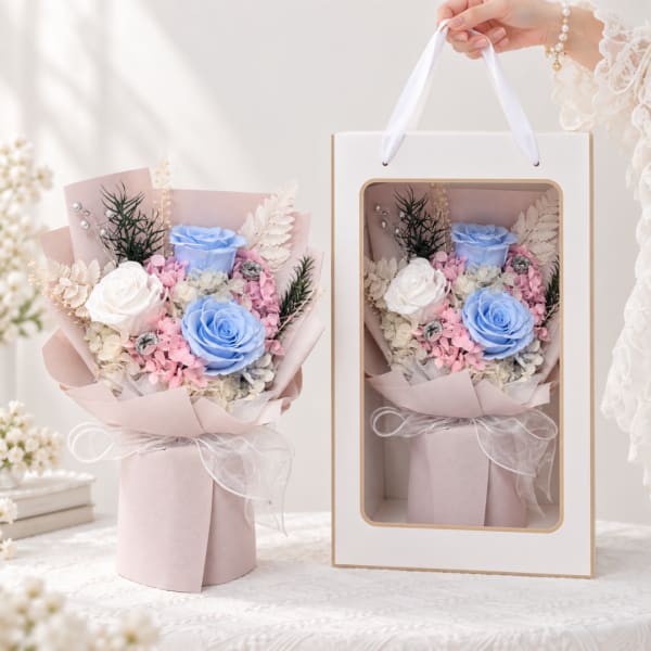 Bouquet of blue and white roses in pink wrapping, shown beside a gift box