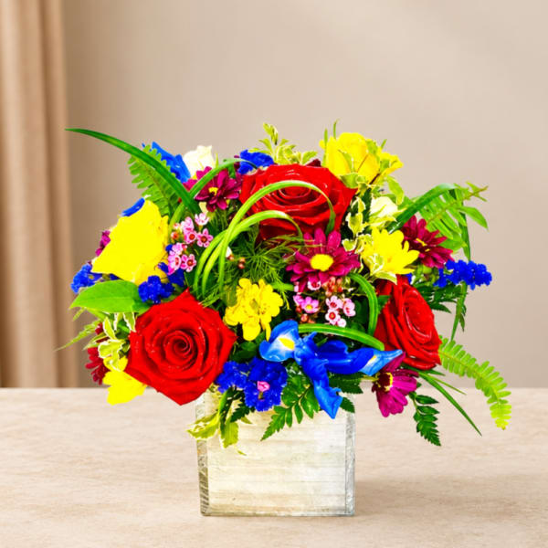 Bright mixed bouquet with red roses in a square glass vase