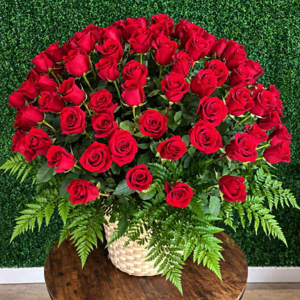 Large bouquet of red roses in a woven basket with fern foliage