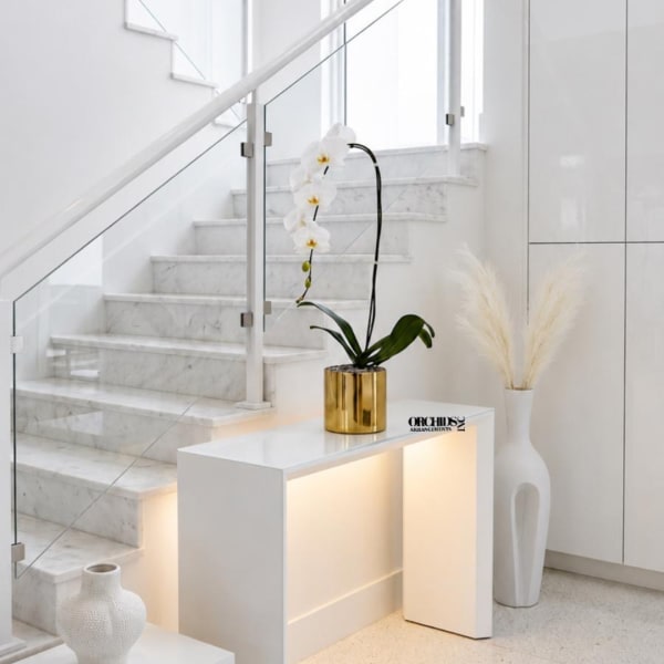 White orchid arrangement in a gold pot on a white table