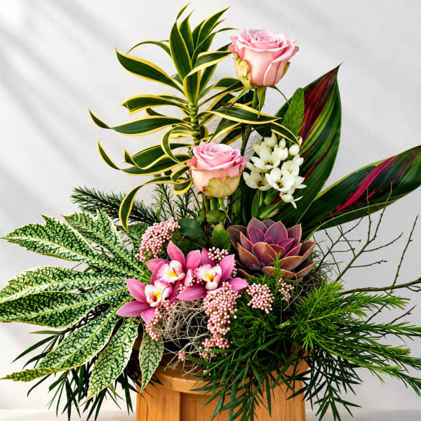 Tropical floral arrangement with pink roses, orchids, and succulents in a wooden container