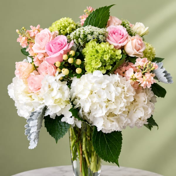 Pink and white roses with hydrangeas in a clear glass vase