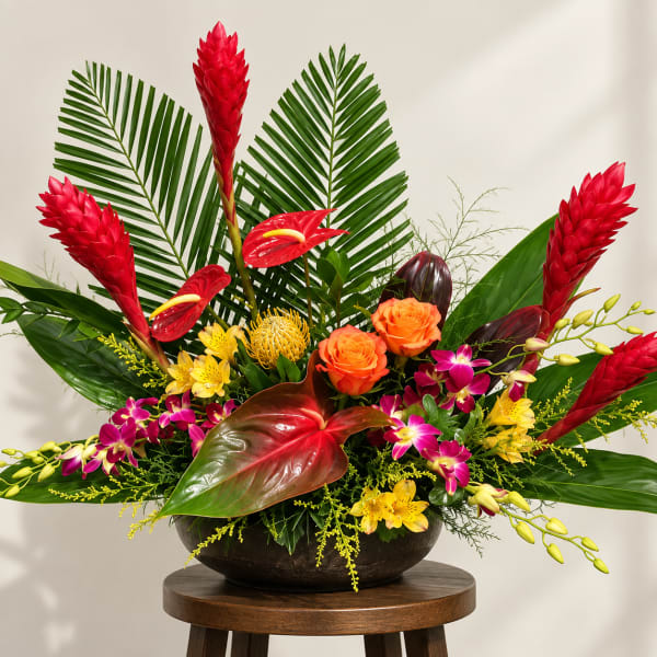 Tropical arrangement with red ginger, orange roses, and orchids in a dark bowl vase