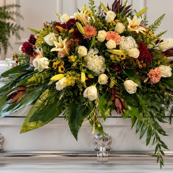 Large floral casket spray with white roses, lilies, and burgundy blooms