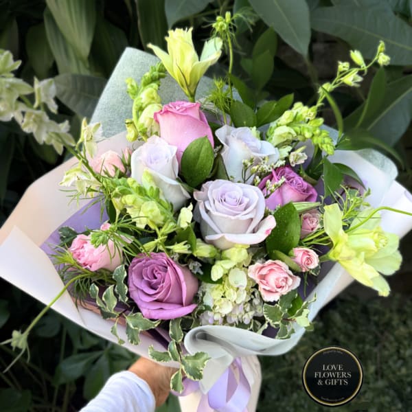 Handheld bouquet of pastel roses and pale yellow flowers wrapped in white paper