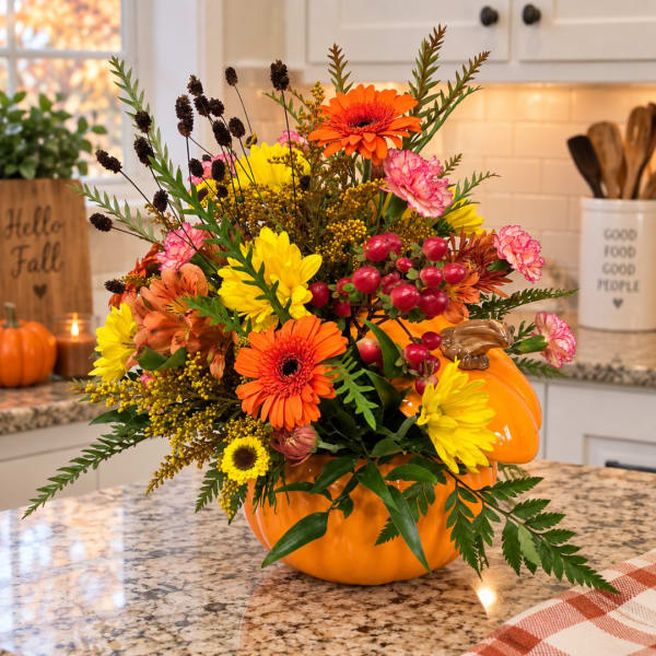 Fall floral arrangement in a pumpkin-shaped container with orange, yellow, and pink blooms