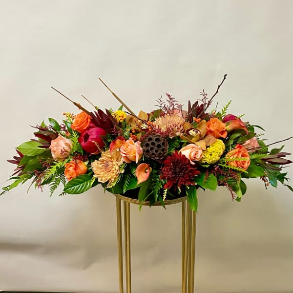 Low floral centerpiece with orange and burgundy blooms in a gold stand
