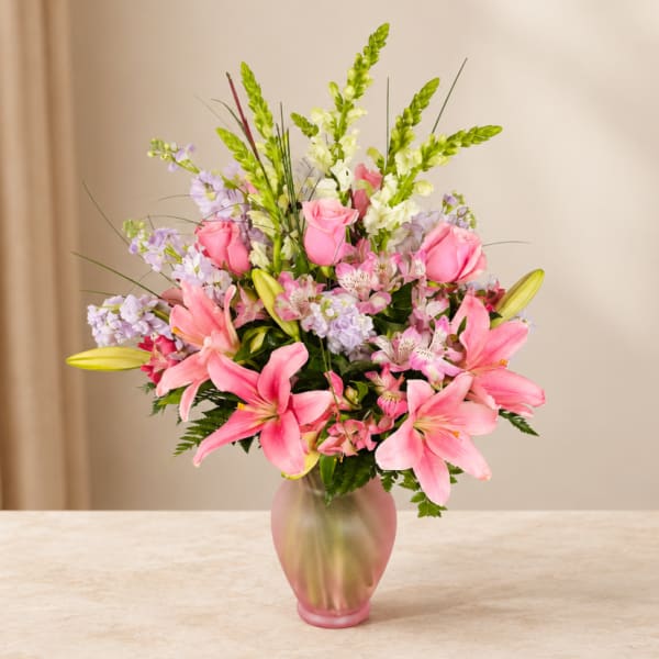Pink lilies and roses arranged in a frosted glass vase