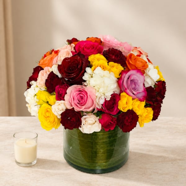 Mixed bouquet of roses in a green glass vase beside a small candle