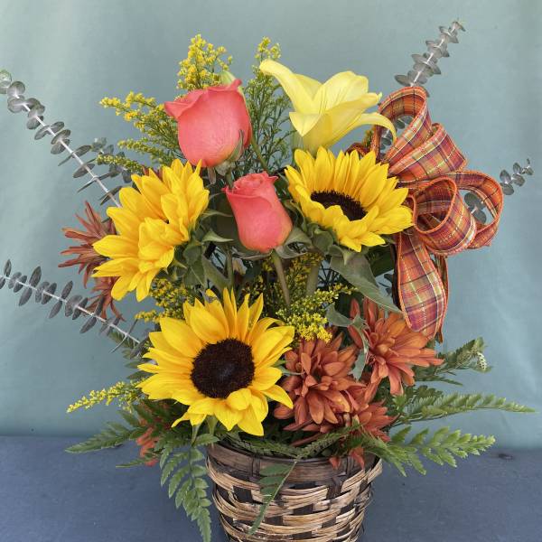 Basket arrangement with sunflowers, pink roses, and a yellow lily with plaid ribbon
