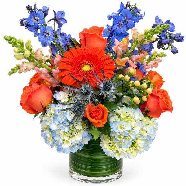 Bright mixed bouquet in a glass vase with orange, blue, and pale blooms
