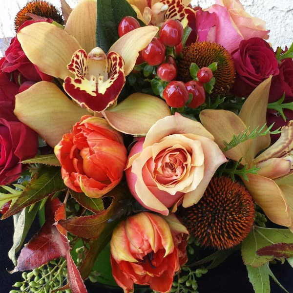 Mixed bouquet with roses, tulips, and orchids in warm red and peach tones