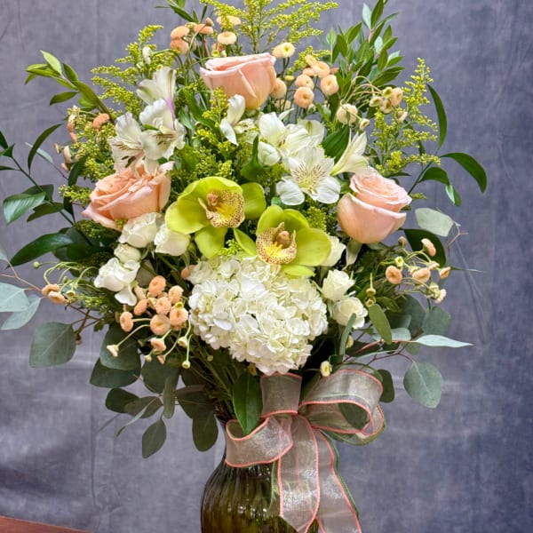 Peach roses, white hydrangea, and green orchids in a glass vase with ribbon