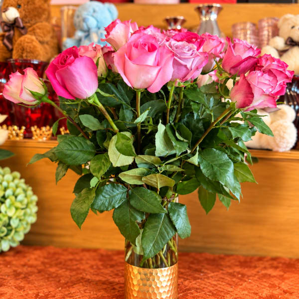 Pink roses arranged in a clear glass vase with a gold base