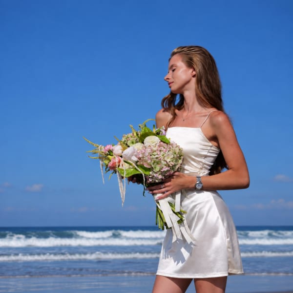 Woman in a white dress holding a pastel bouquet on a beach